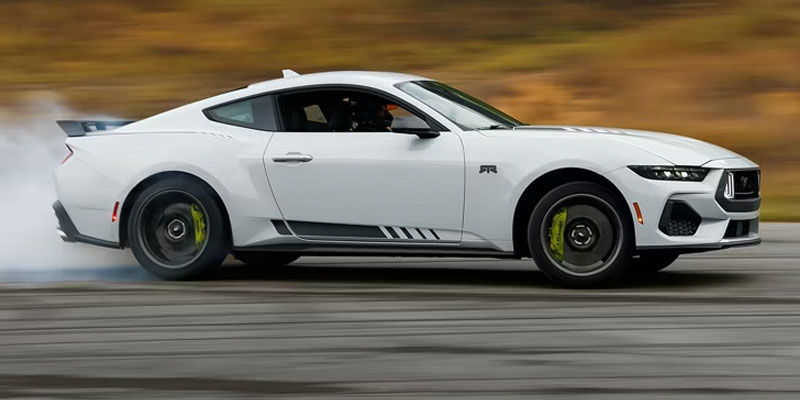 White Ford Mustang drifting on a track, emitting tire smoke.